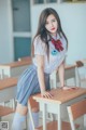 A woman in a school uniform leaning on a desk.