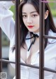 A woman in a white shirt and black bow tie leaning against a fence.