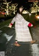 A woman walking down a street at night in a plaid coat.