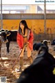 A woman in a red jacket is holding a pitchfork in front of cows.