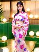 A woman in a pink kimono standing in front of a green wall.