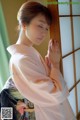 A woman in a pink kimono leaning against a window.