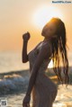 A woman in a white dress standing in the ocean at sunset.