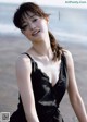 A woman in a black dress posing on the beach.