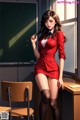 A woman in a red suit standing in front of a blackboard.