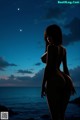 A nude woman standing on a rock by the ocean at night.