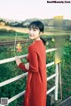 A woman in a red dress leaning against a fence.