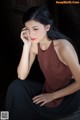 A woman sitting on a wooden bench with her hand on her chin.