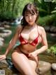 A woman in a red bikini sitting on a rock in the water.