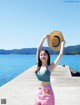 A woman standing on a pier holding a straw hat.