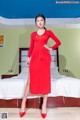 A woman in a red dress standing on a bed.