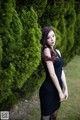 A woman in a black dress standing in front of a tree.