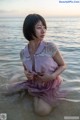 A woman in a pink dress sitting in the water.