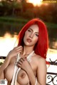 A woman with red hair posing naked on a bridge.