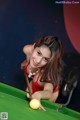 A woman in a red dress is playing pool.