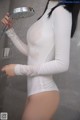 A woman in a white bodysuit is holding a shower head.